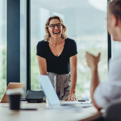 Businesswoman standing at conference table and laughing. Female professional smiling during a meeting in office boardroom.